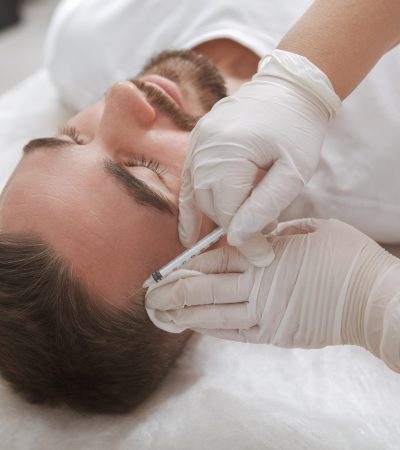 Unrecognizable professional trichologist giving hairloss injections treatment to male client